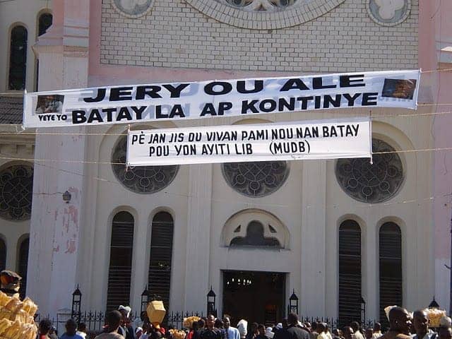 Father-Gerard-Jean-Juste’s-funeral-National-Cathedral-0609-banner-‘Gerry-you-are-gone-but-the-struggle-will-go-on’-by-Sasha-Kramer, Jounen jèn, Days of Remembrance, World News & Views 